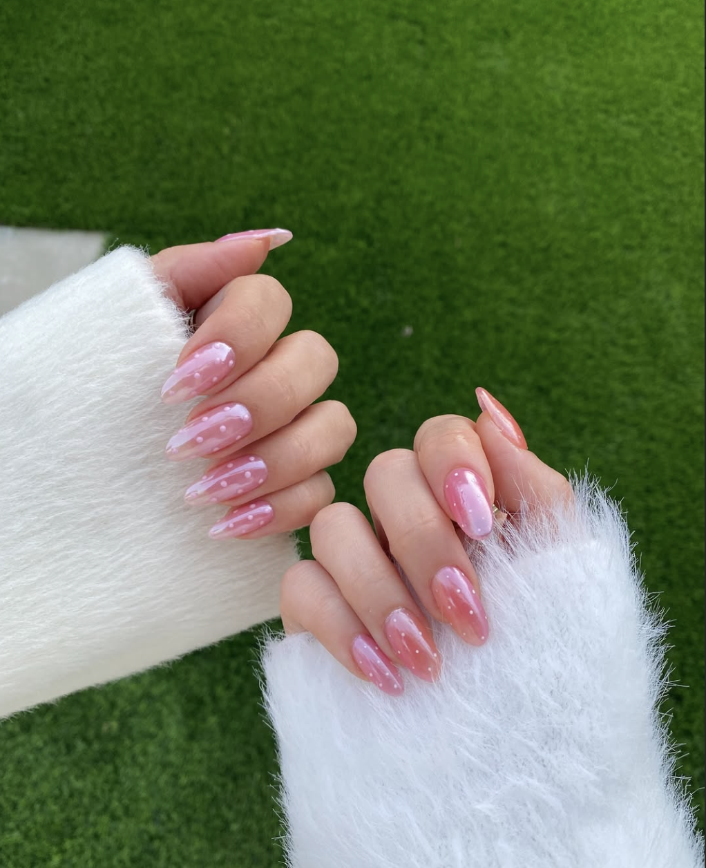 Alt Text: A close-up of short, rounded nails featuring a shimmering pink "glazed strawberry" finish with delicate white micro-dots.