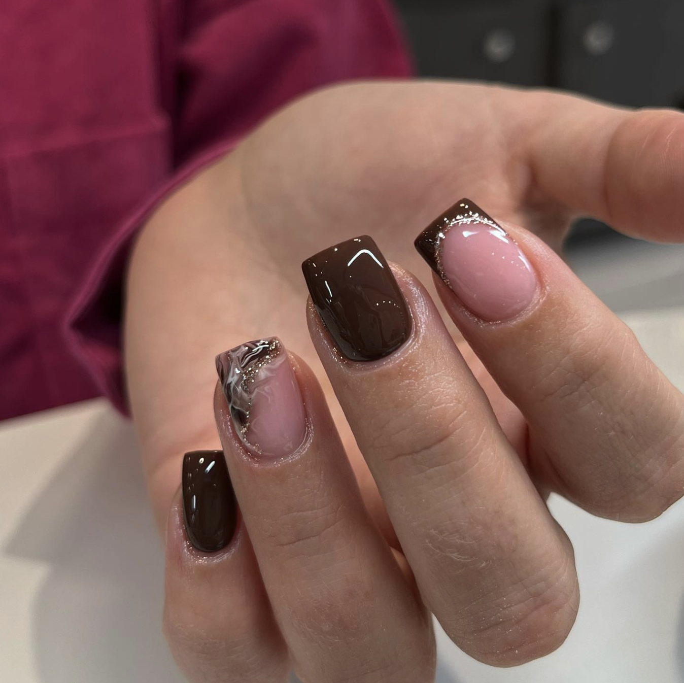 A close-up of short, square nails featuring a mix of solid chocolate brown polish and matching brown French tips on a sheer pink base.