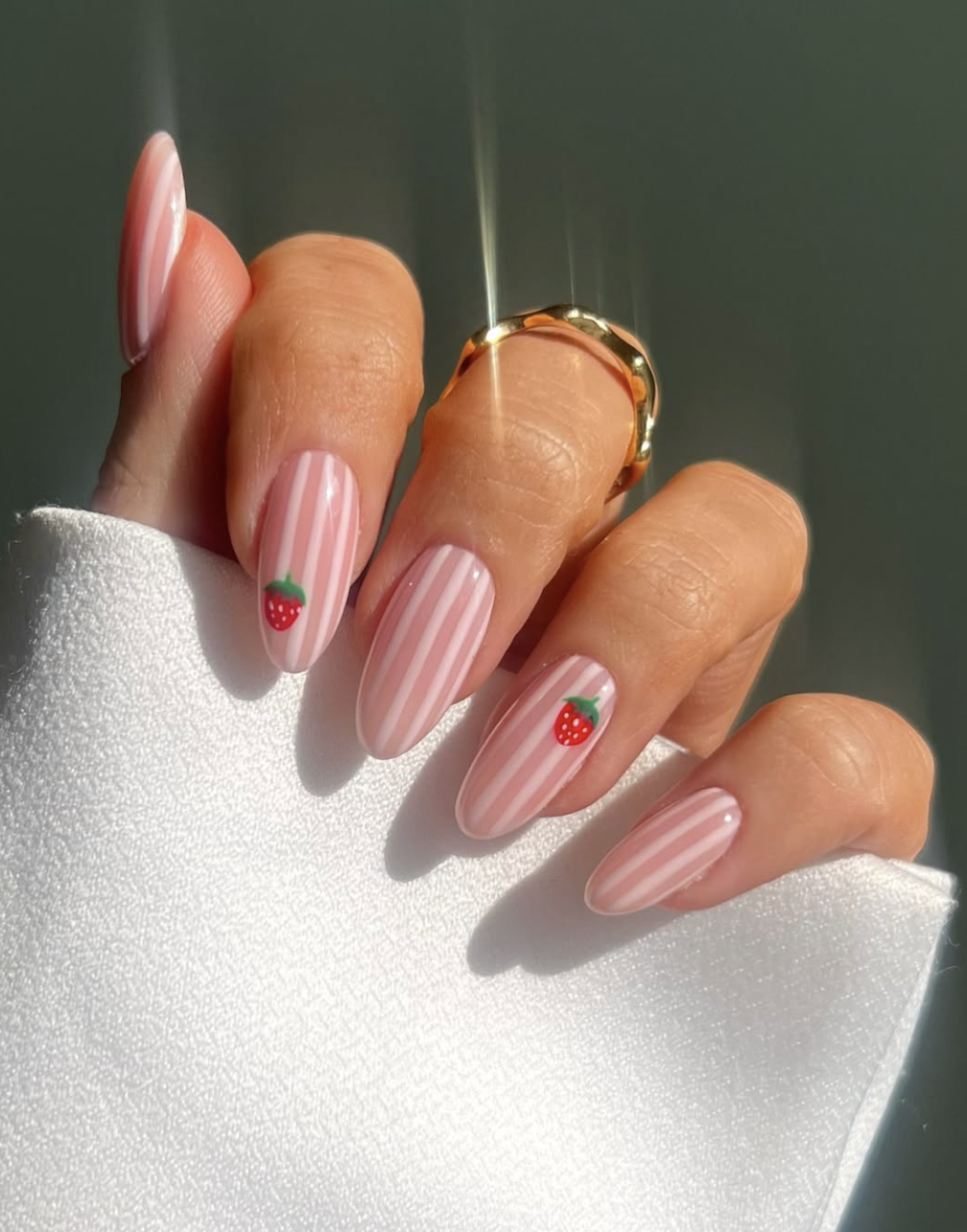 high-feminine spring manicure by @iolapallade_beauty featuring almond nails with light and dark pink vertical stripes and tiny hand-painted strawberry accents.