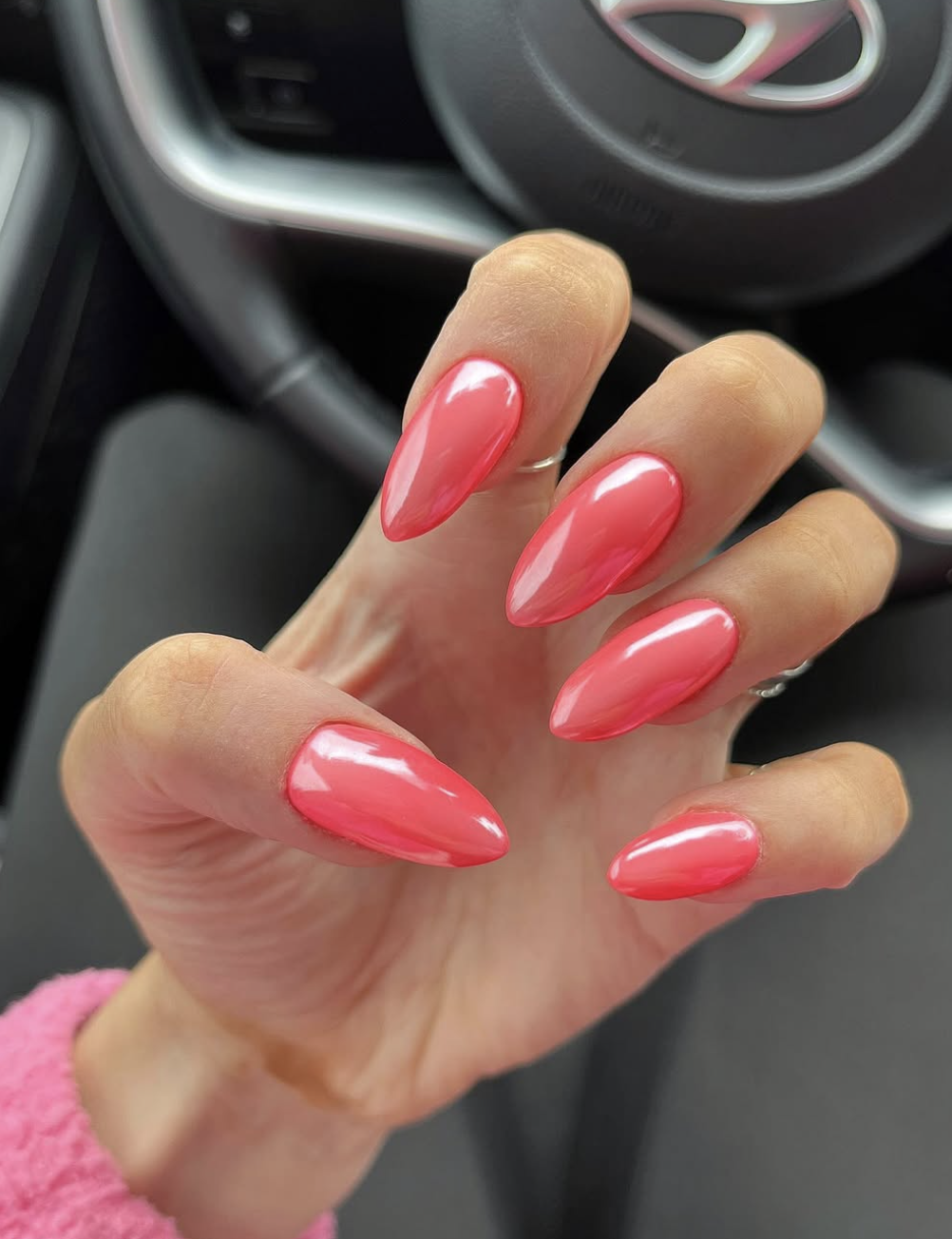 A close-up of long almond-shaped nails with a vibrant watermelon pink base and a high-shine chrome finish.