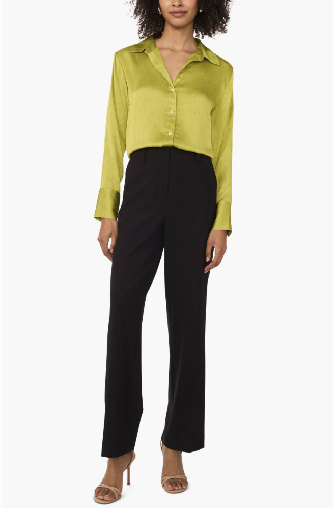 A woman wearing a vibrant lime green textured satin button-up shirt tucked into high-waisted black tailored trousers, representing a polished "Zoom-ready" top for a hybrid work capsule wardrobe.