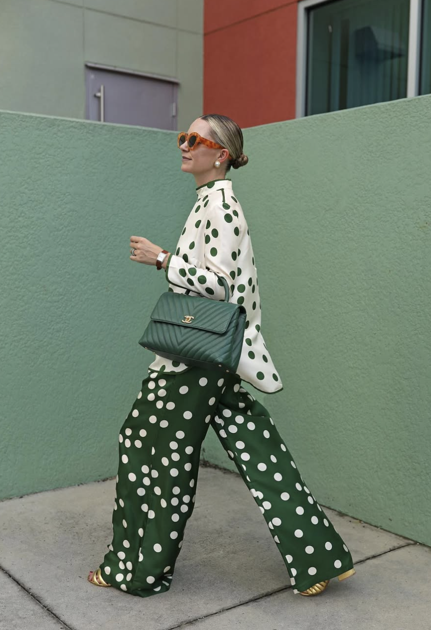 woman in green and white polka dot button-down shirt untucked over matching wide leg pants with a Chanel bag