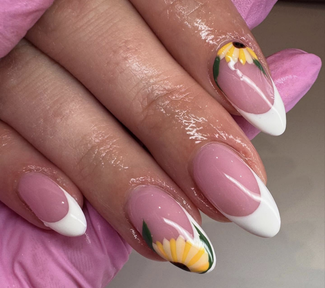 Long almond-shaped nails with a crisp white French tip, featuring a hand-painted sunflower and green leaves curving along the side of the nail bed.