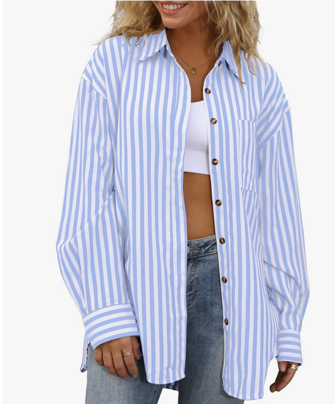 A close-up view of a woman wearing an oversized blue and white vertical striped boyfriend shirt with brown buttons, styled open over a white crop top and denim jeans.