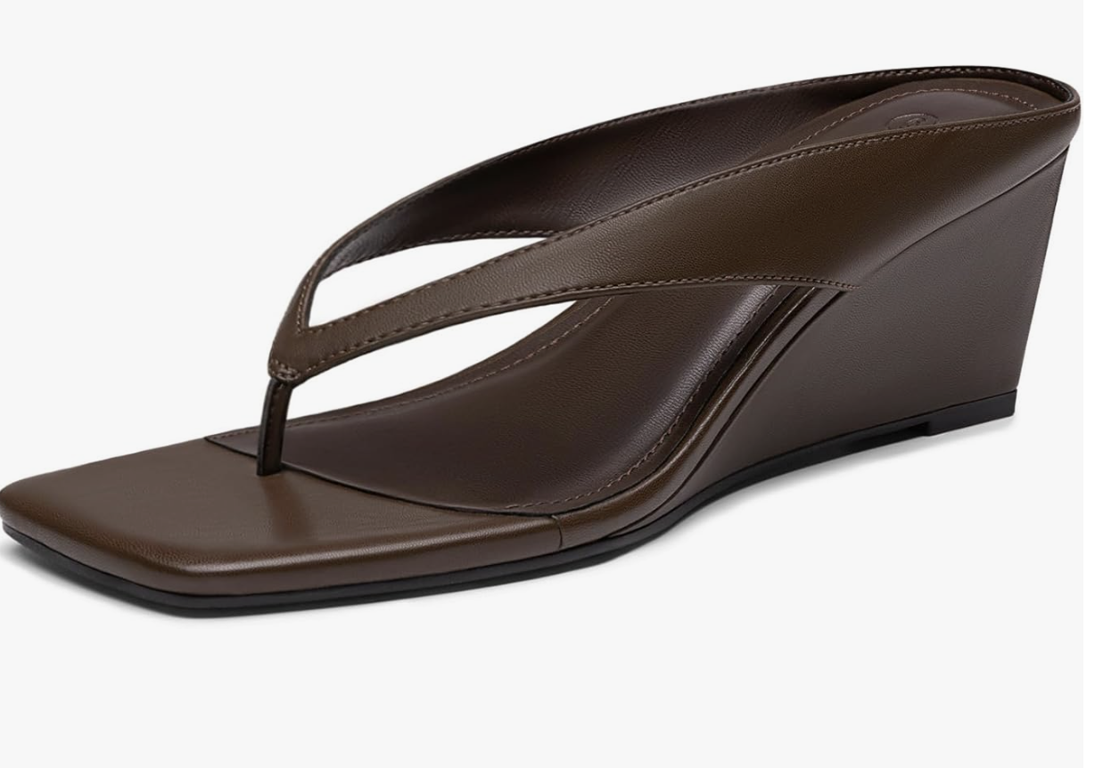 A close-up of a pair of chocolate brown leather low wedge flip-flops with a square toe and a minimalist thong strap, representing the elevated footwear trend for Spring 2026.