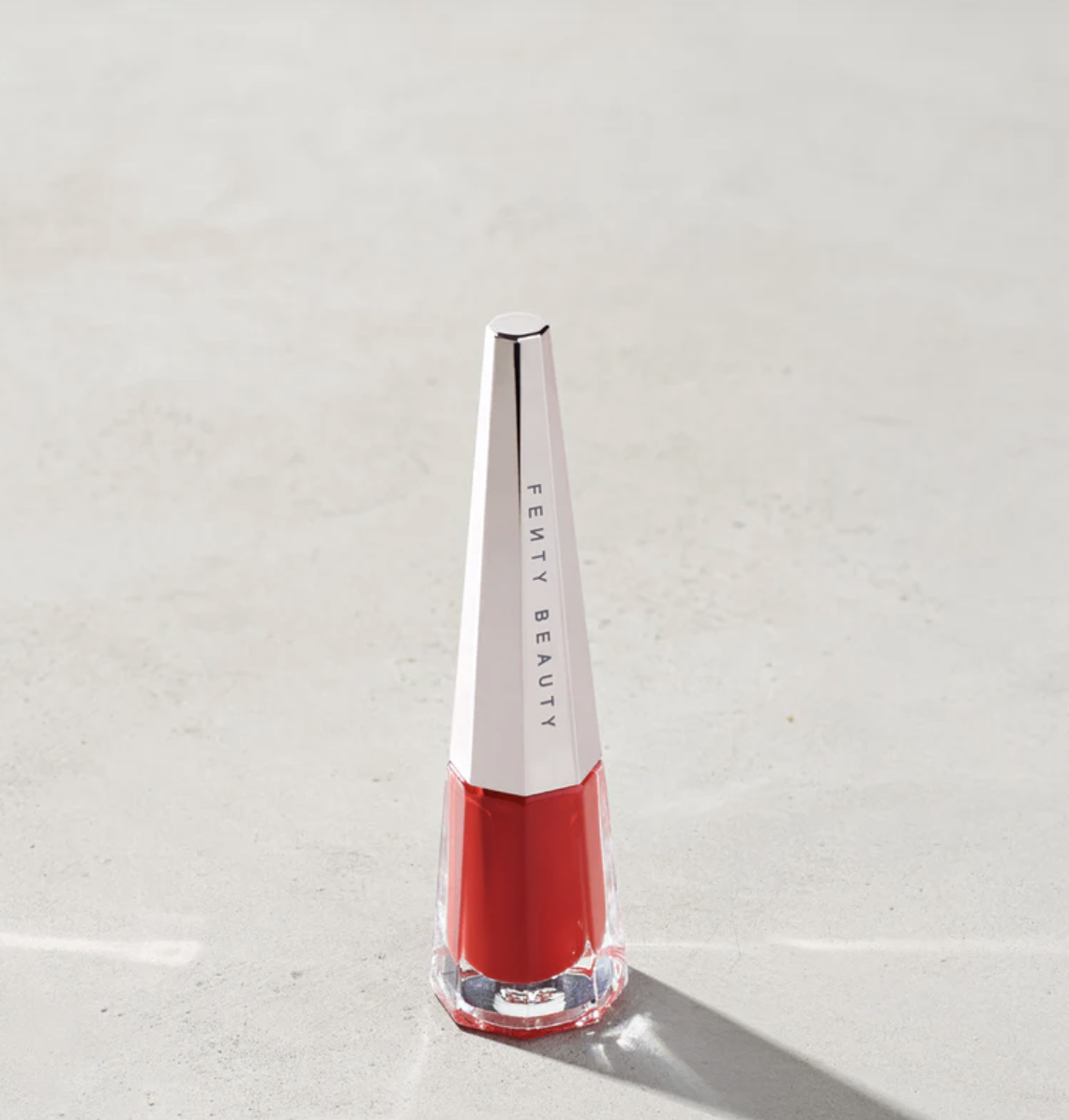 A close-up shot of the architectural glass bottle of Fenty Beauty Stunna Lip Paint in the shade Uncensored, showcasing a soft, fluid true red liquid lipstick ideal for a Summer palette.