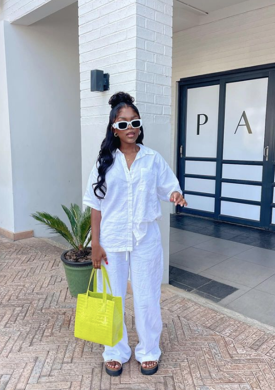 Woman wearing a chic white linen pants outfit with a matching button-down shirt and a lime green tote bag for summer.