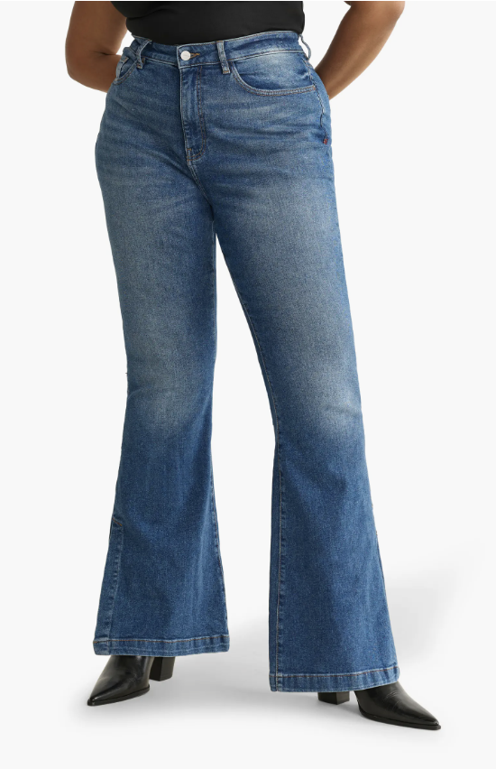 A person with an hourglass figure wearing Warp + Weft Mia high-rise flare jeans in a dark wash, showing the split-hem detail and the balanced silhouette created by the flared leg.