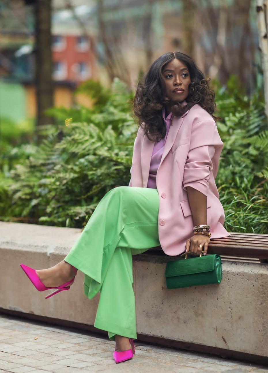 A woman wearing a light pink oversized blazer with vibrant lime green wide-leg trousers and hot pink pointed-toe heels.
