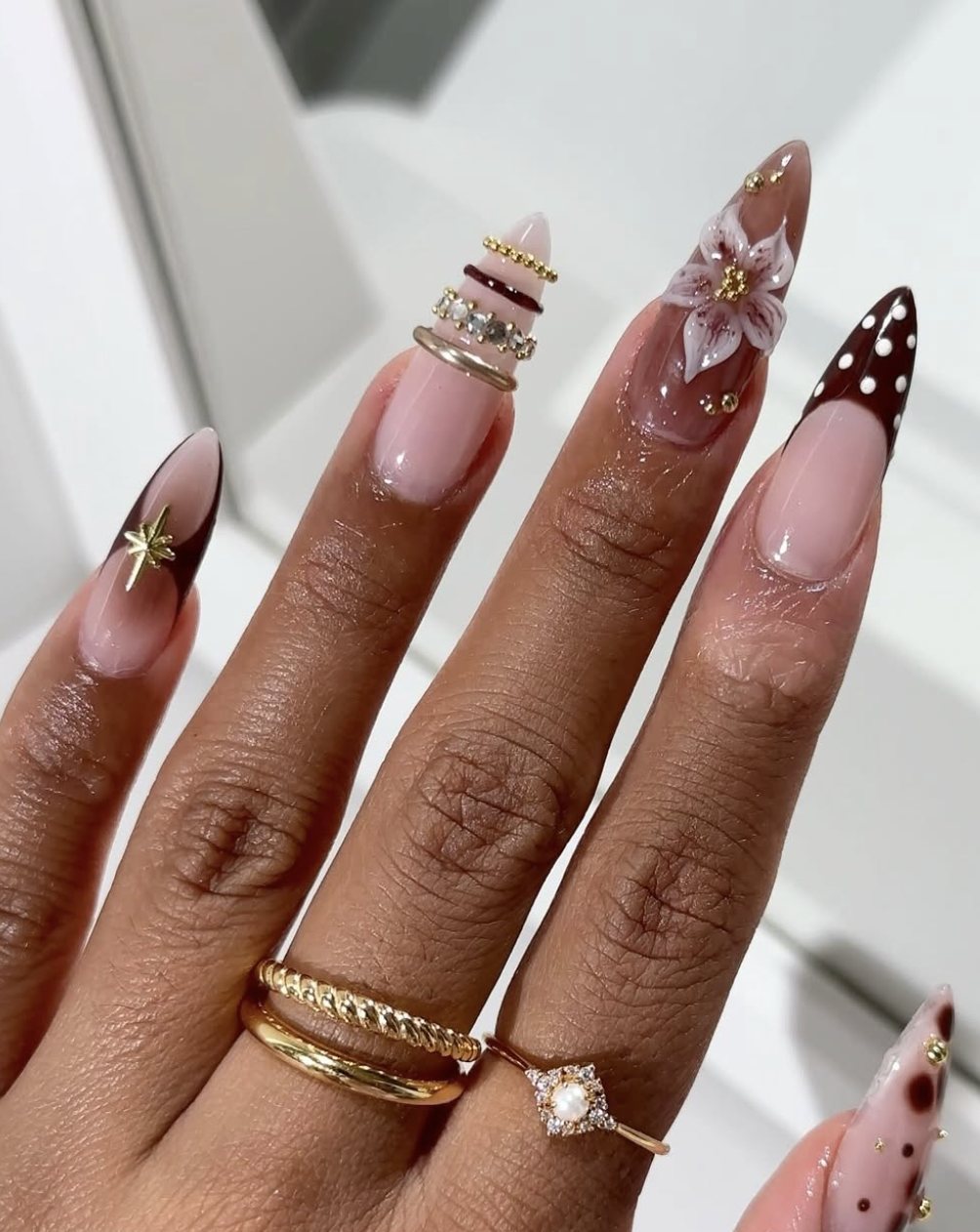 Nude almond nails with layered 3D gold and silver textured bangle bands and a large gold star charm.