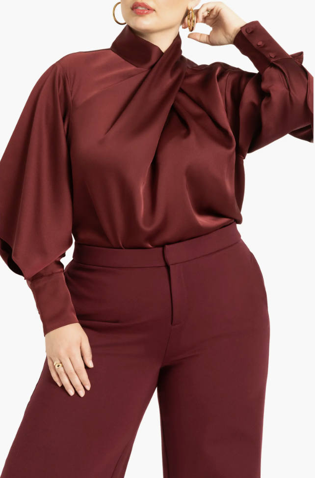 Woman wearing an ELOQUII burgundy draped-neck satin blouse paired with matching burgundy tailored trousers