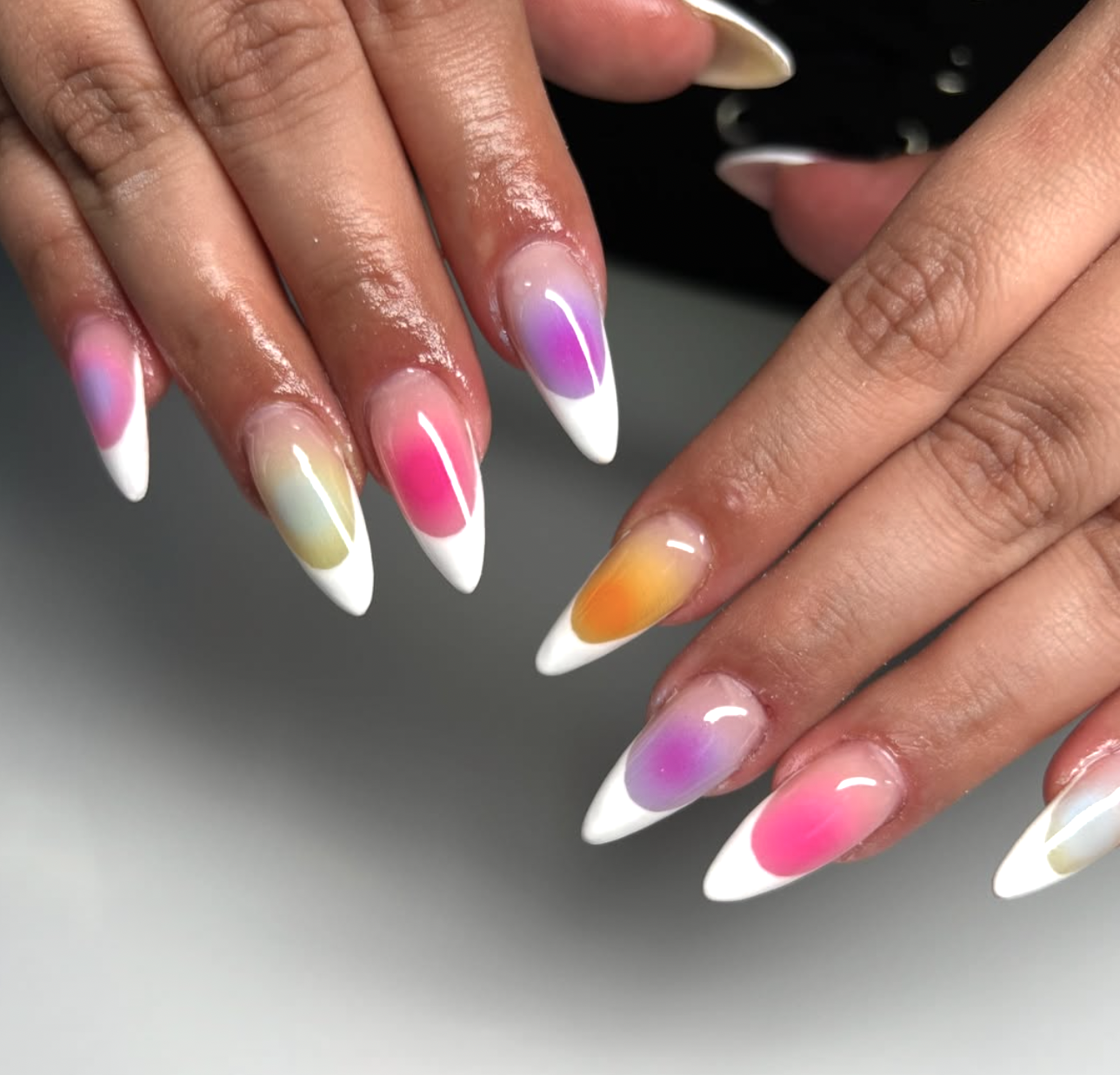 Long almond-shaped nails featuring a hazy, airbrushed aura center in shades of purple, pink, and orange, finished with a crisp white French tip.
