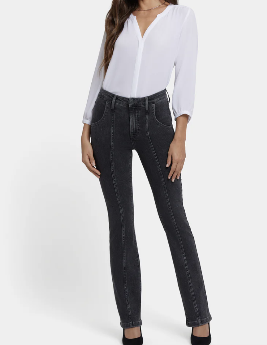 A person with an hourglass figure wearing slate grey NYDJ Billie Mini Bootcut Petite jeans, featuring a slimming center seam and a subtle flare that balances the hips.