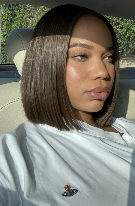 A woman with a sleek, chin-length brown bob and a middle part, wearing a white t-shirt and showcasing the prominent cheekbones of a diamond face shape.