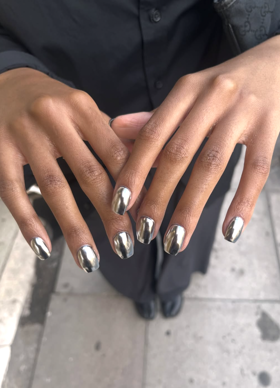 A close-up of a hand with short nails featuring a reflective, metallic silver chrome finish.