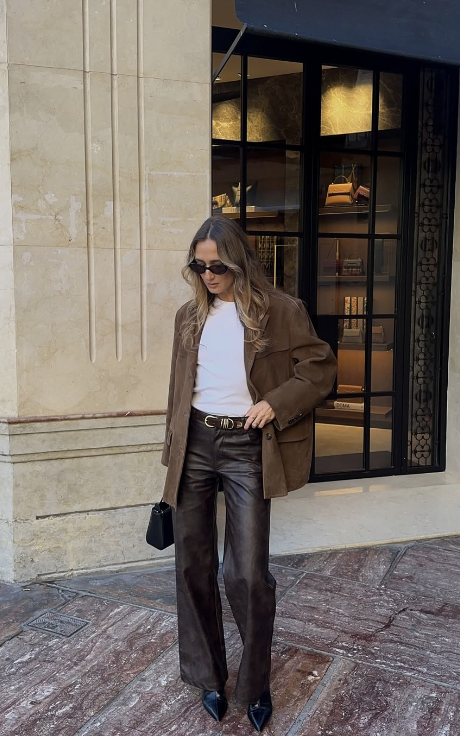 Woman wearing brown wide-leg leather pants, white t-shirt and brown suede blazer with a black belt