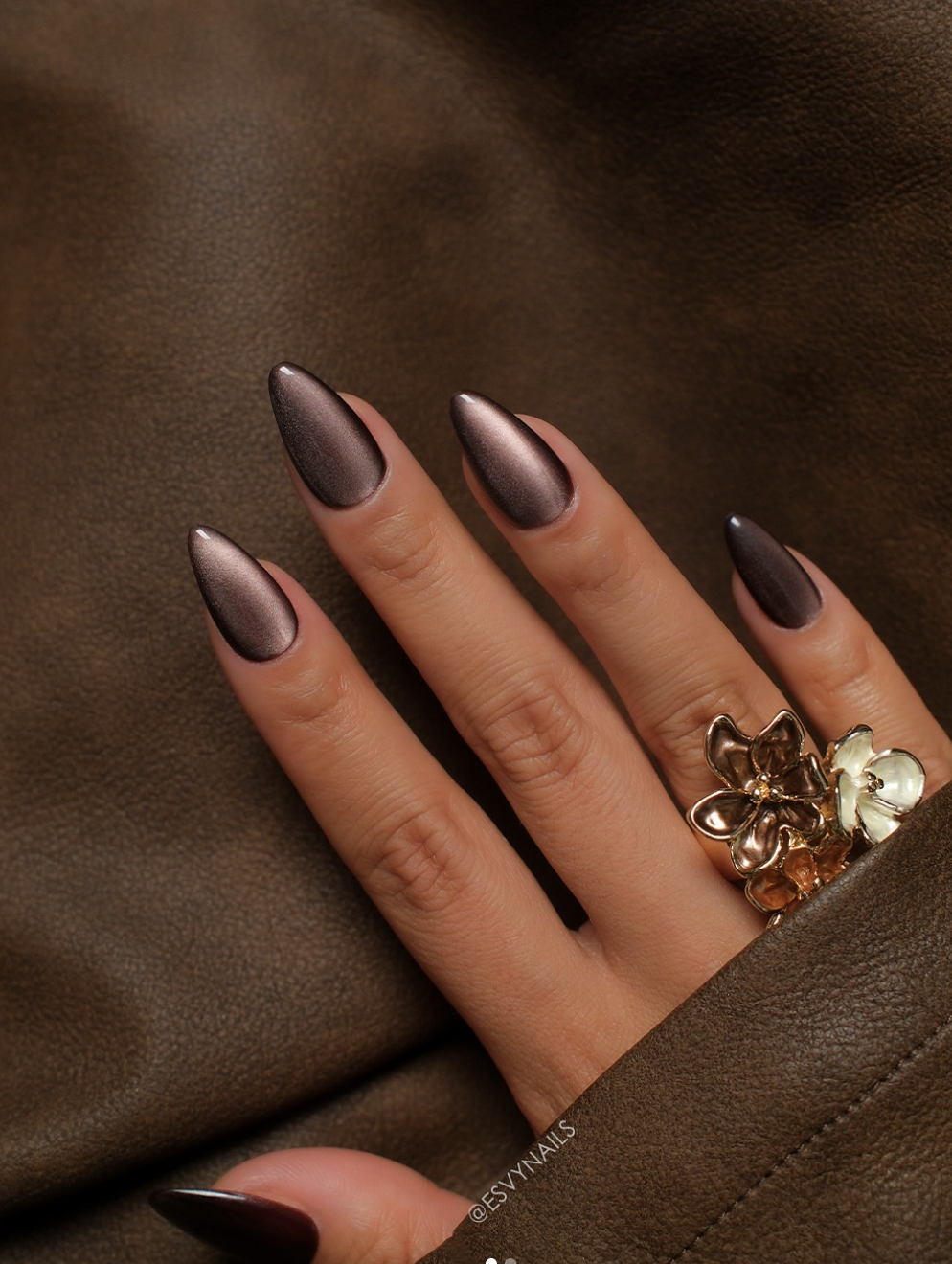 Close-up of a hand with long, almond-shaped nails showcasing a mesmerizing summer cat-eye manicure with a glossy deep espresso brown magnetic polish that creates a dimensional, light-catching metallic stripe across each nail.