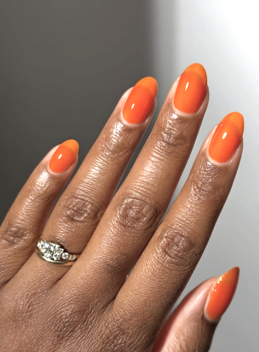Long oval nails with a vibrant, glossy tangerine orange polish, showcasing bold and cute June nail ideas.