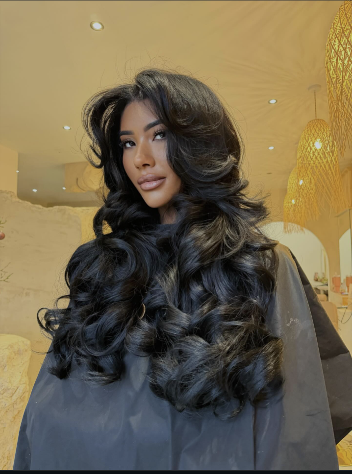 A woman with long dark hair styled in a bouncy, layered butterfly haircut blowout.