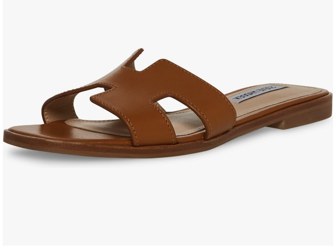 A pair of cognac brown genuine leather slide sandals featuring a sophisticated H-shaped cutout strap and a lightly padded sole, styled as a chic spring essential for women in their 50s.