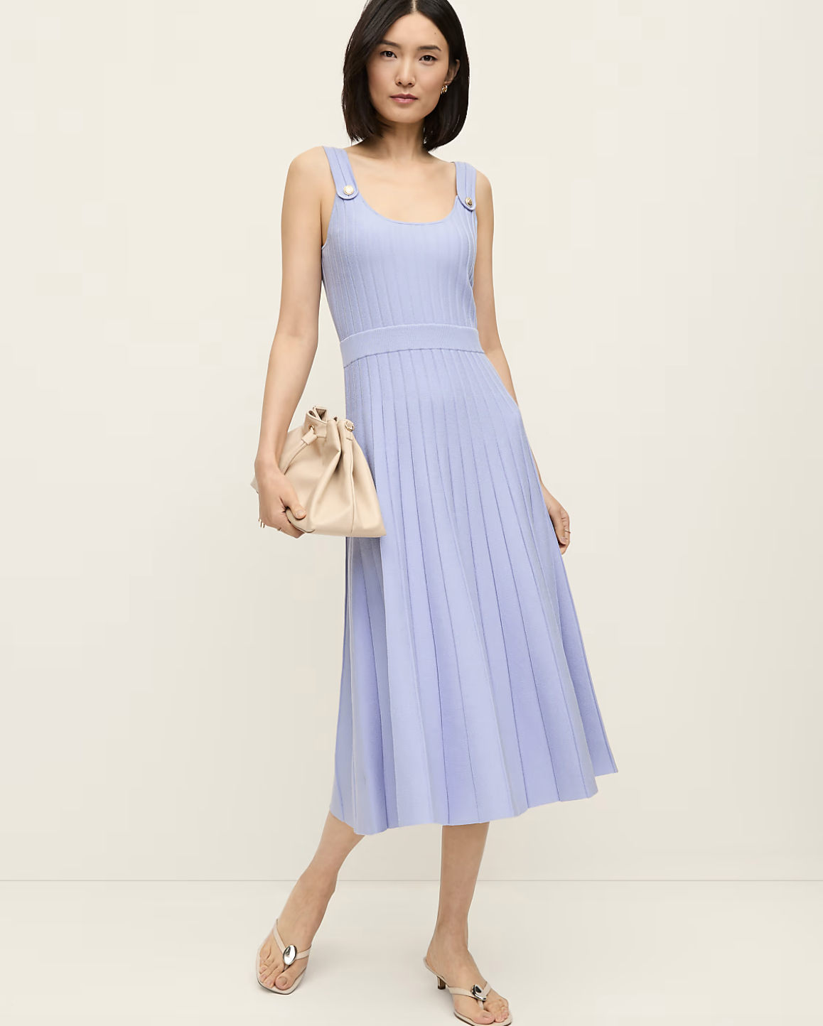 A close-up view of a lavender pleated midi dress paired with metallic strappy kitten heel mules featuring a distinct circle embellishment on the front strap.
