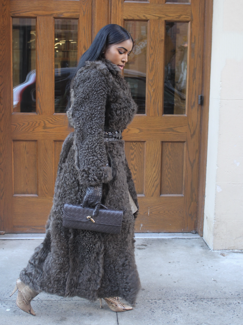 A pro stylist-inspired look featuring a long textured fur coat layered over a neutral dress and strappy heels.
