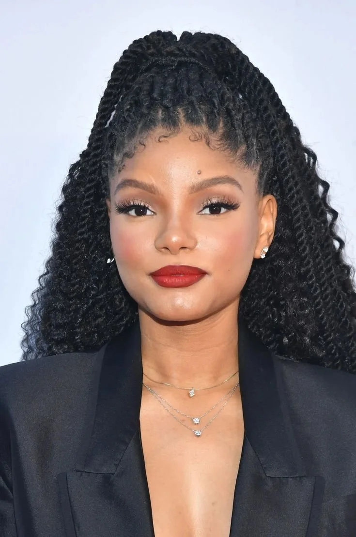 Halle Bailey with long, textured passion twists styled in a half-up ponytail with a side part, highlighting how the side-swept fringe balances a heart face shape.