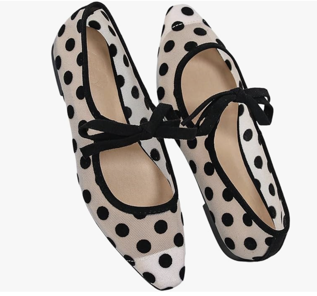 A close-up of a white oversized button-down jacket with large black polka dots, styled with a thin brown leather belt and black trousers.