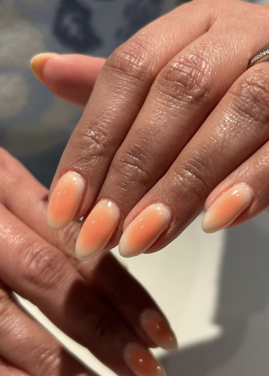 A close-up of long, almond-shaped aura nails featuring a soft milky-white base with a vibrant, airbrushed neon peach and orange glowing center.