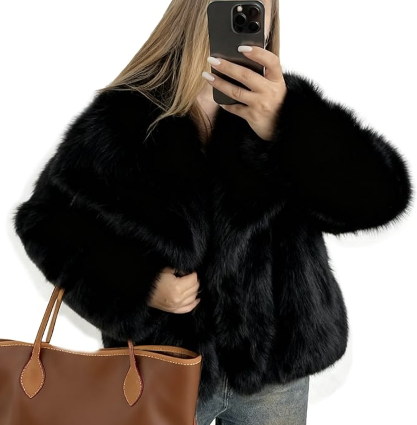 Woman taking a mirror selfie wearing a plush, oversized black faux fur jacket and holding a brown leather tote bag.