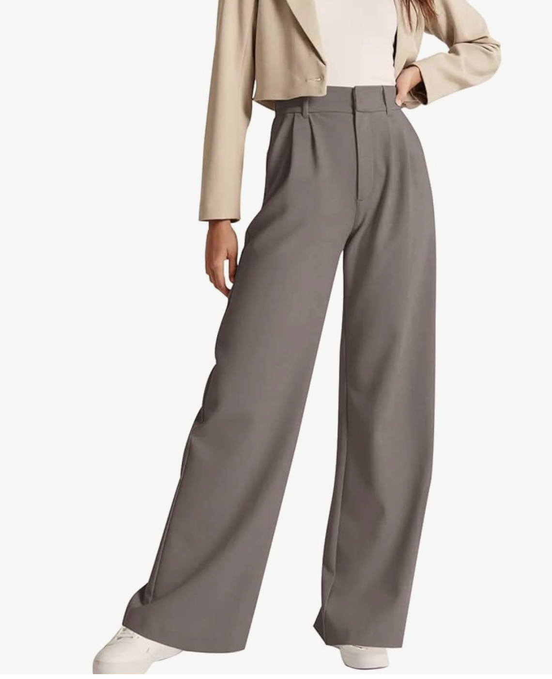 t: A close-up view of a person wearing high-waisted, pleated wide-leg trousers in taupe grey styled with clean white sneakers.