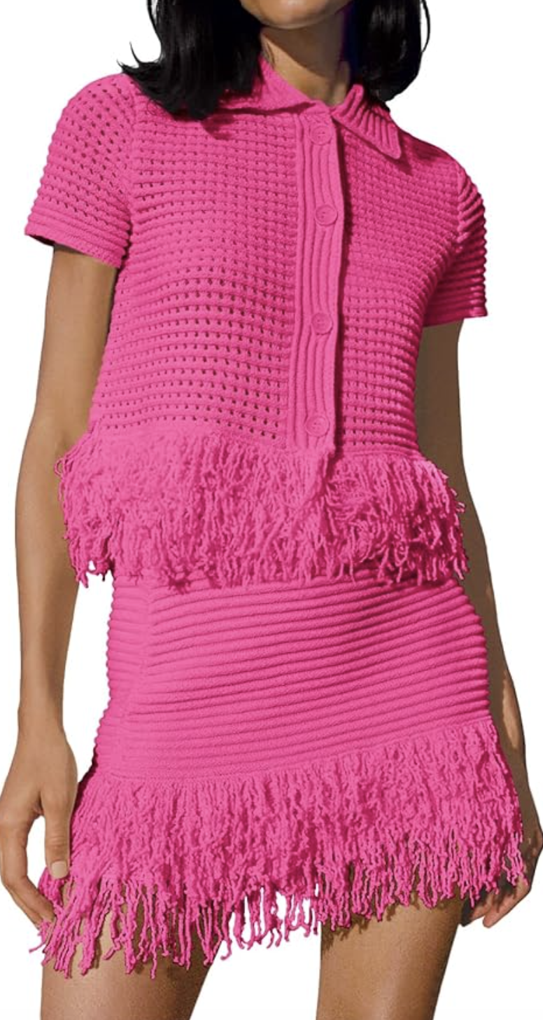 A woman wearing a bright pink short-sleeved crochet mini dress with fringe trim along the midsection and hem.