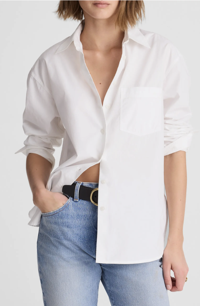 A close-up style shot of a woman wearing light wash straight-leg denim jeans paired with a tucked-in white button-down shirt and a black textured leather belt with a gold buckle.