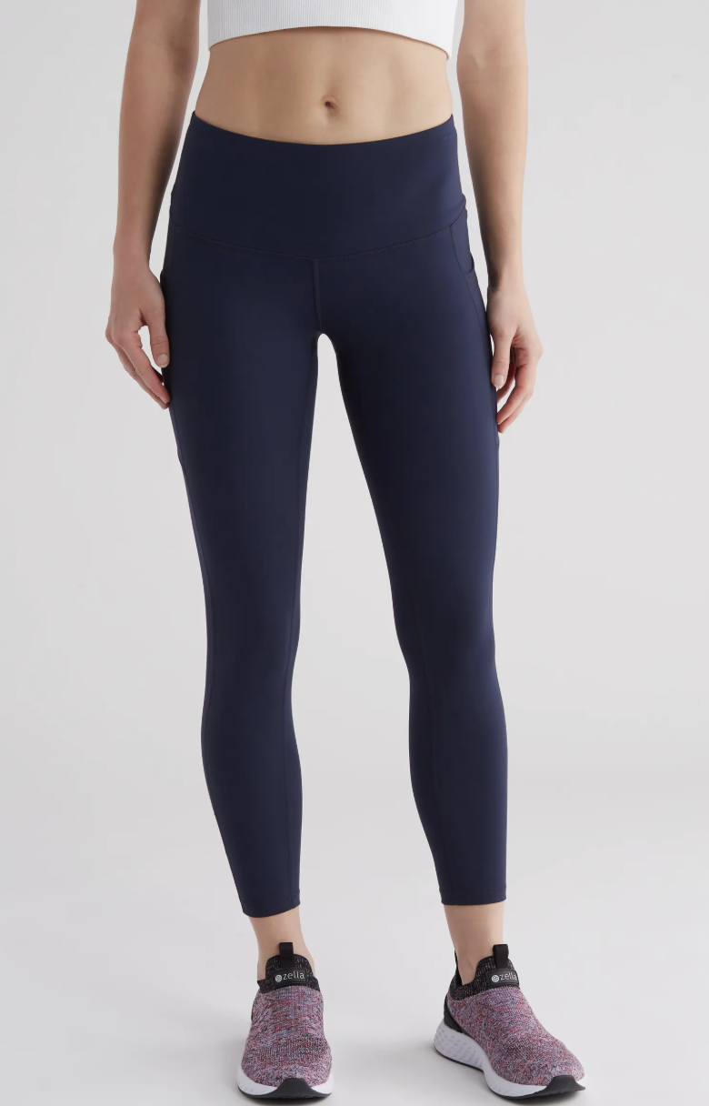 A model wearing the Zella Live In High Waist Pocket 7/8 Leggings in navy blue, featuring a streamlined high-rise fit and functional side pockets, perfect for petite styling in 2026.
