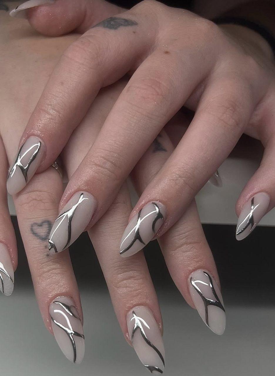 Long, almond-shaped nails featuring a glossy, semi-sheer nude base coat decorated with fluid, liquid-like 3D silver chrome abstract line work.