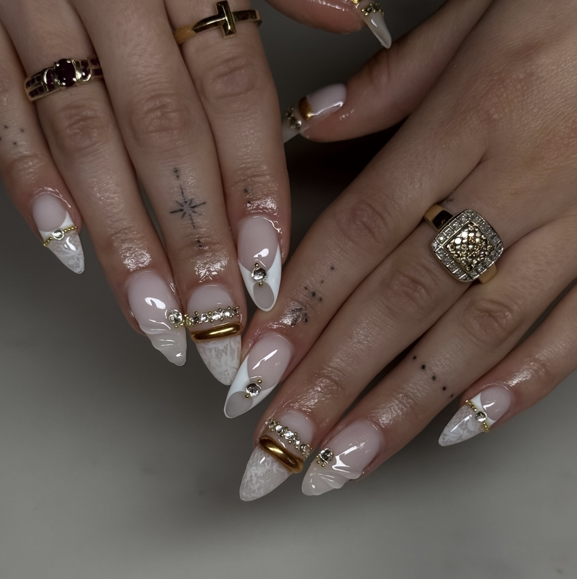 Almond nails with milky white base, white marble French tips, and thick 3D gold bands with inset crystals.