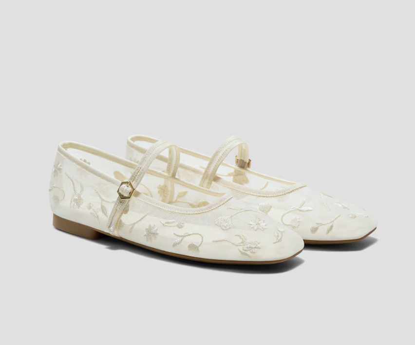 A pair of white mesh Mary Jane flats featuring delicate cream floral embroidery and a thin gold buckle strap, showcasing the feminine square-toe trend for Spring 2026.