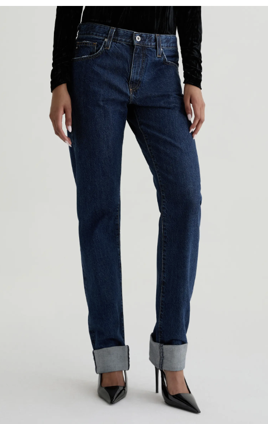 A person with an hourglass figure wearing AG The Boyfriend mid-rise relaxed straight-leg jeans in a light vintage wash, styled with black pointed-toe heels to elongate the silhouette.