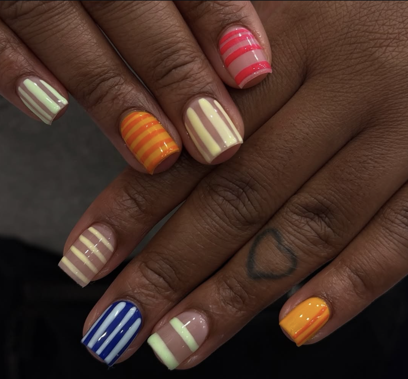 Short, rounded natural nails featuring a playful, multi-colored vertical stripe pattern in vibrant shades of orange, yellow, pink, baby blue, and sage green.