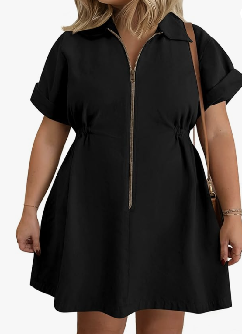 A woman wearing a black short-sleeve shirt dress with a silver zipper-front closure, elastic drawstring waist, and side pockets.