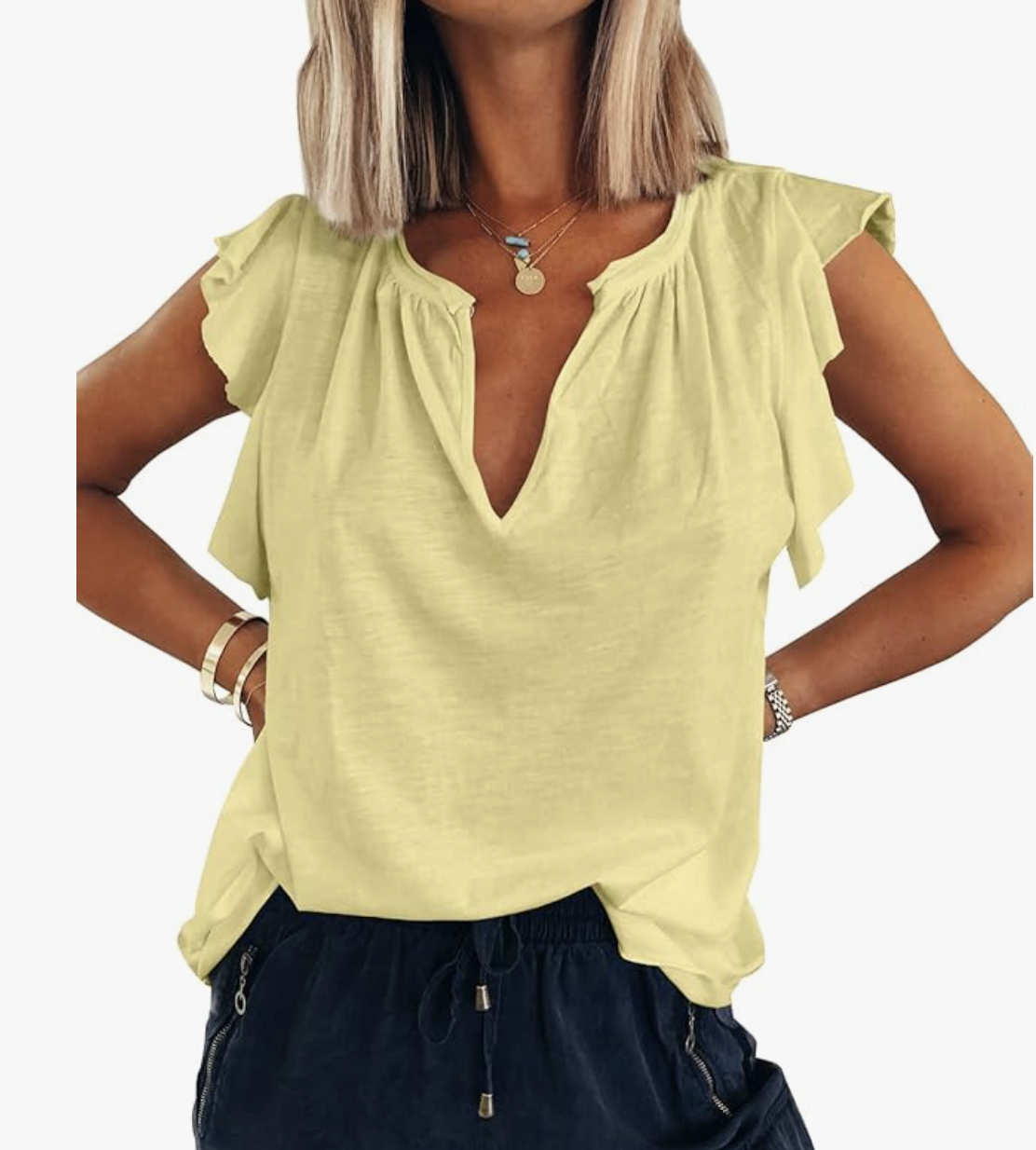 Close-up of a woman wearing a pale yellow V-neck tank top with a soft ruffle trim along the split neckline and cap-style sleeve edges, tucked into dark navy drawstring pants.