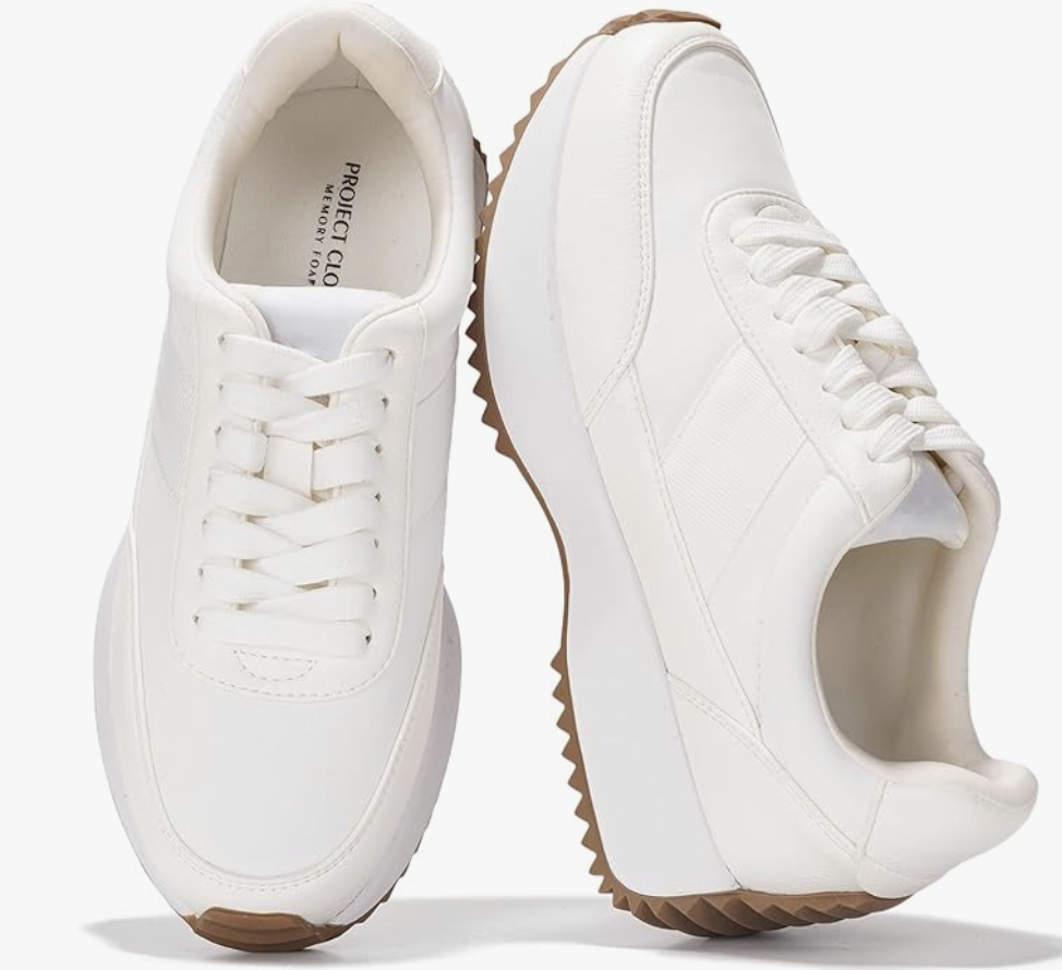 A pair of minimalist white leather sneakers with a gum sole, styled for a professional business casual work outfit.