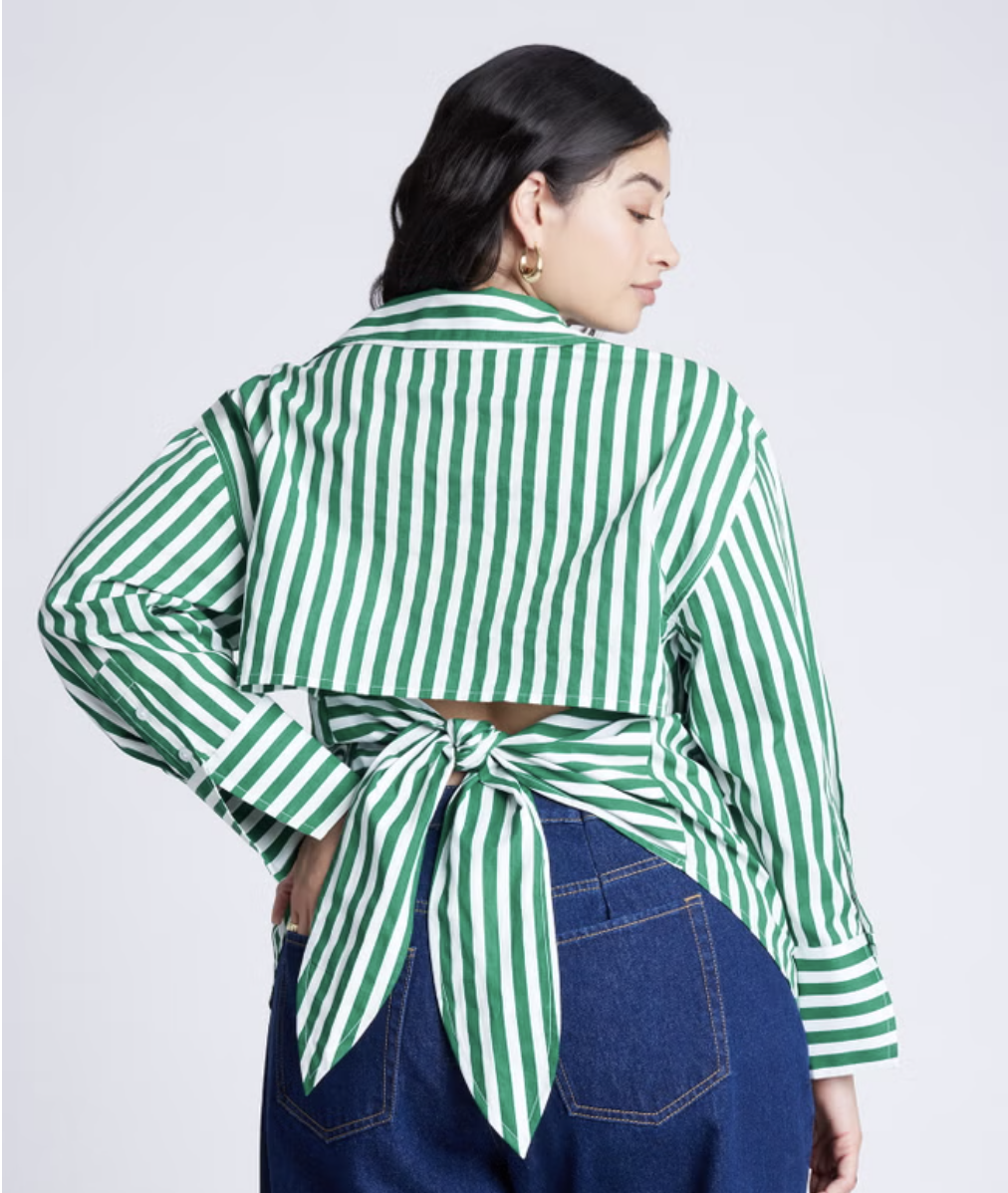 Back view of a woman wearing a green and white striped long-sleeve button-down shirt featuring a cutout back with a large tie-knot detail, paired with blue denim jeans.