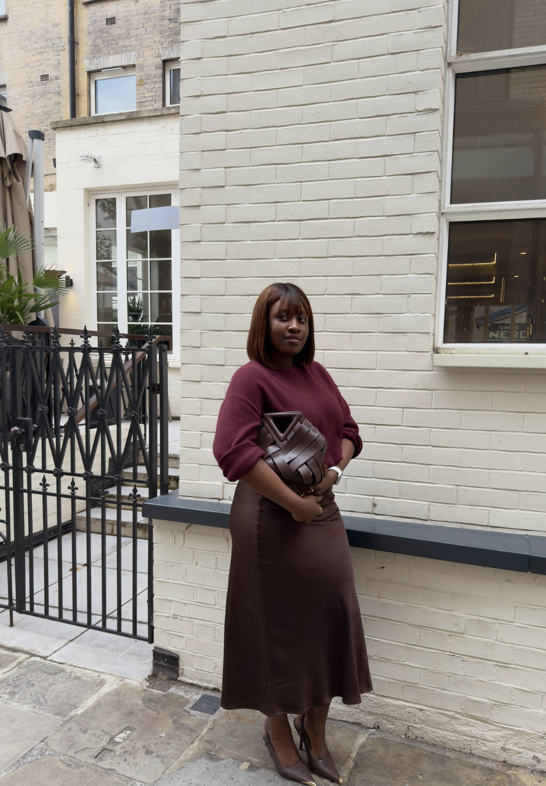 Woman wearing a brown midi skirt with a burgundy sweater, pointed brown heels and a woven bag