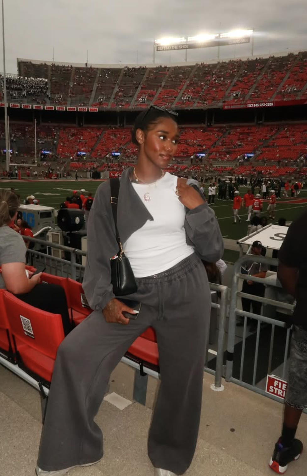 Woman at an Ohio State game wearing a charcoal cropped hoodie and matching wide-leg joggers over a fitted white game-day tee.