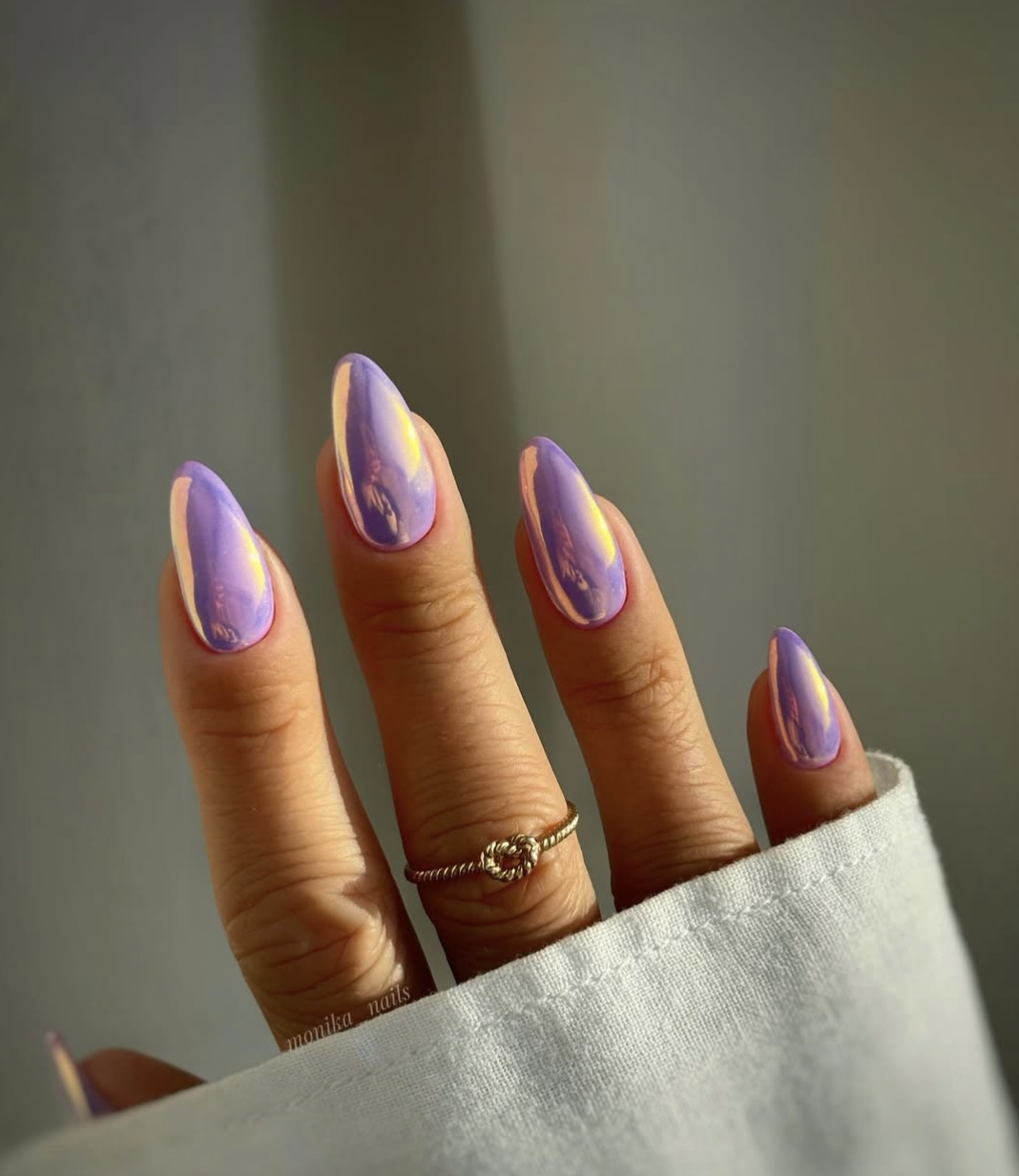 Long, almond-shaped nails showcasing a striking, high-shine purple iridescent chrome finish that flashes gold and pink in the light.
