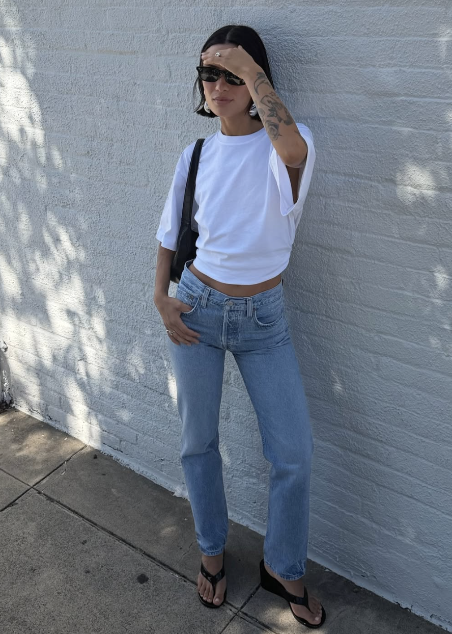 Woman wearing a white t-shirt, light blue cigarette jeans, and black wedge sandals.