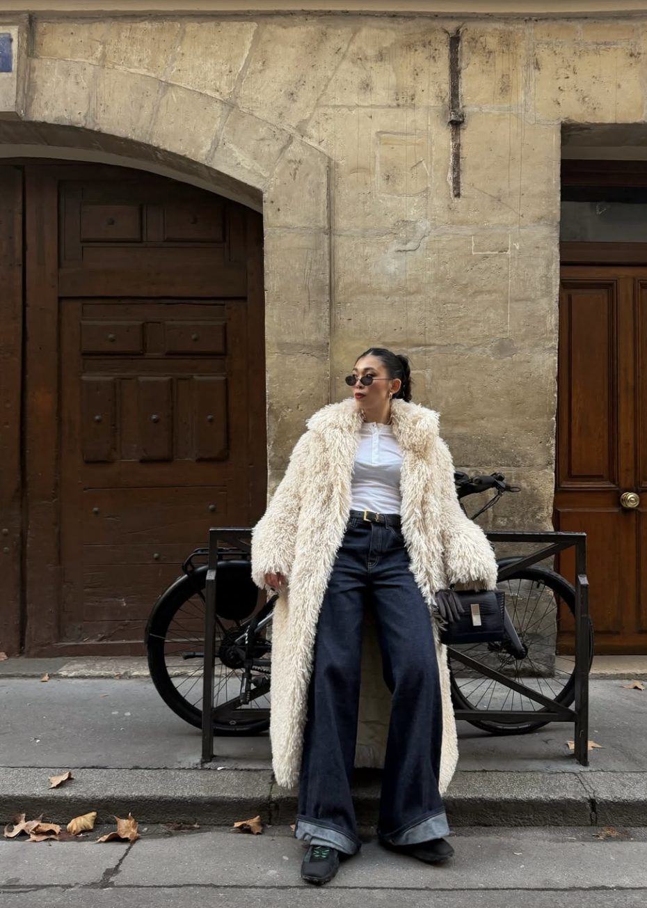 A woman wearing baggy wide-leg jeans paired with a long cream trench coat and black boots to demonstrate the Third Piece Rule for streamlining an oversized silhouette.