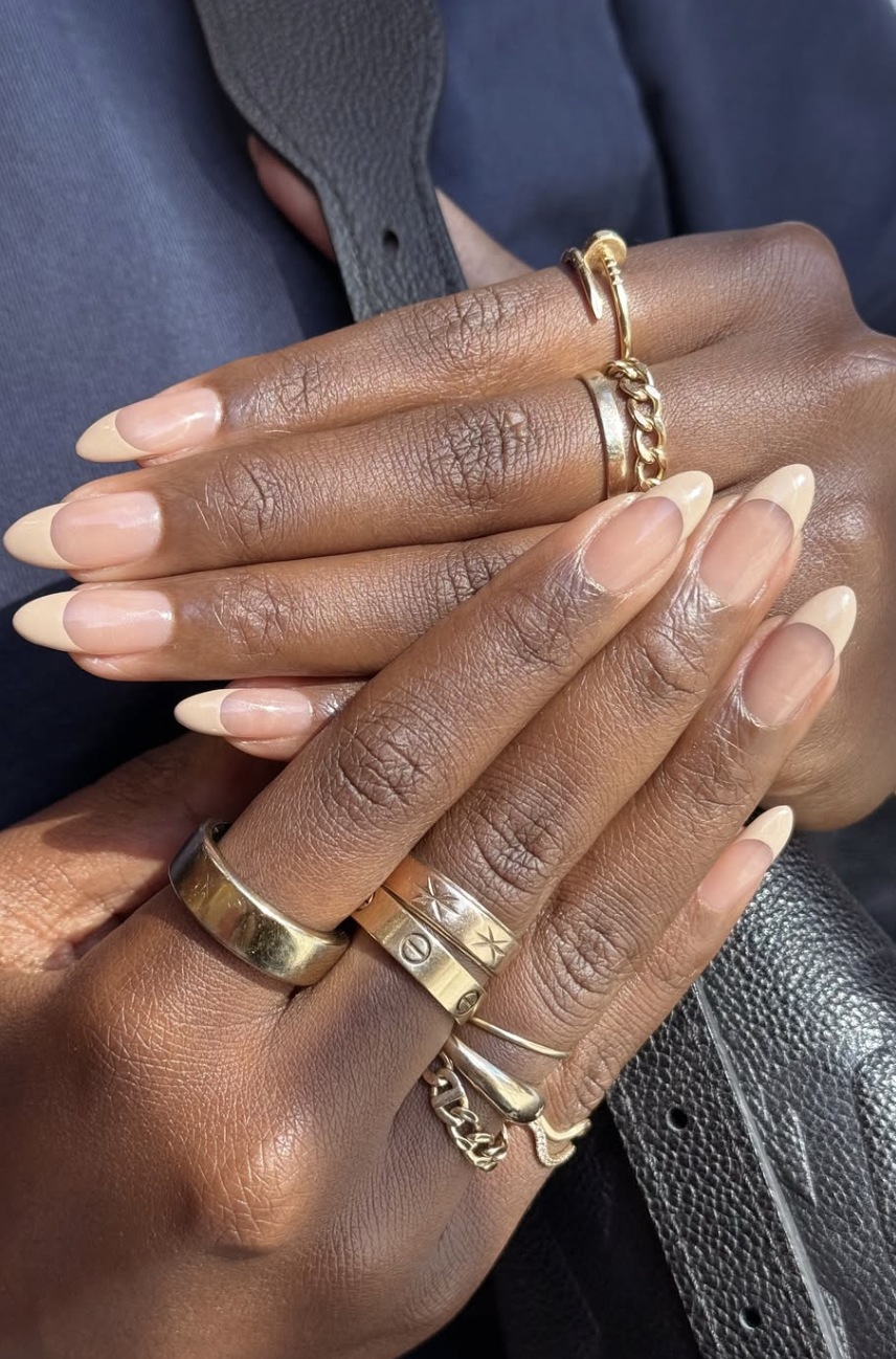 Almond-shaped nails with a sheer nude base and a soft, muted beige French tip finish.