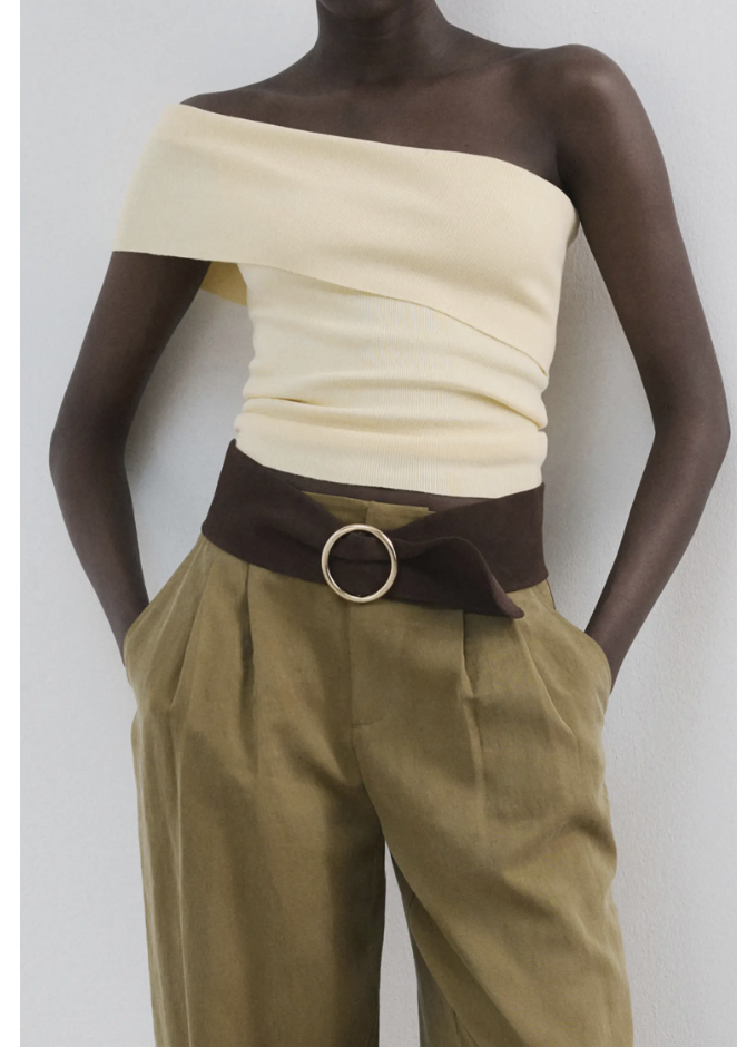 A person wearing a cream-colored off-the-shoulder ribbed long-sleeve top tucked into high-waisted tan cargo pants with a large silver circle buckle belt.